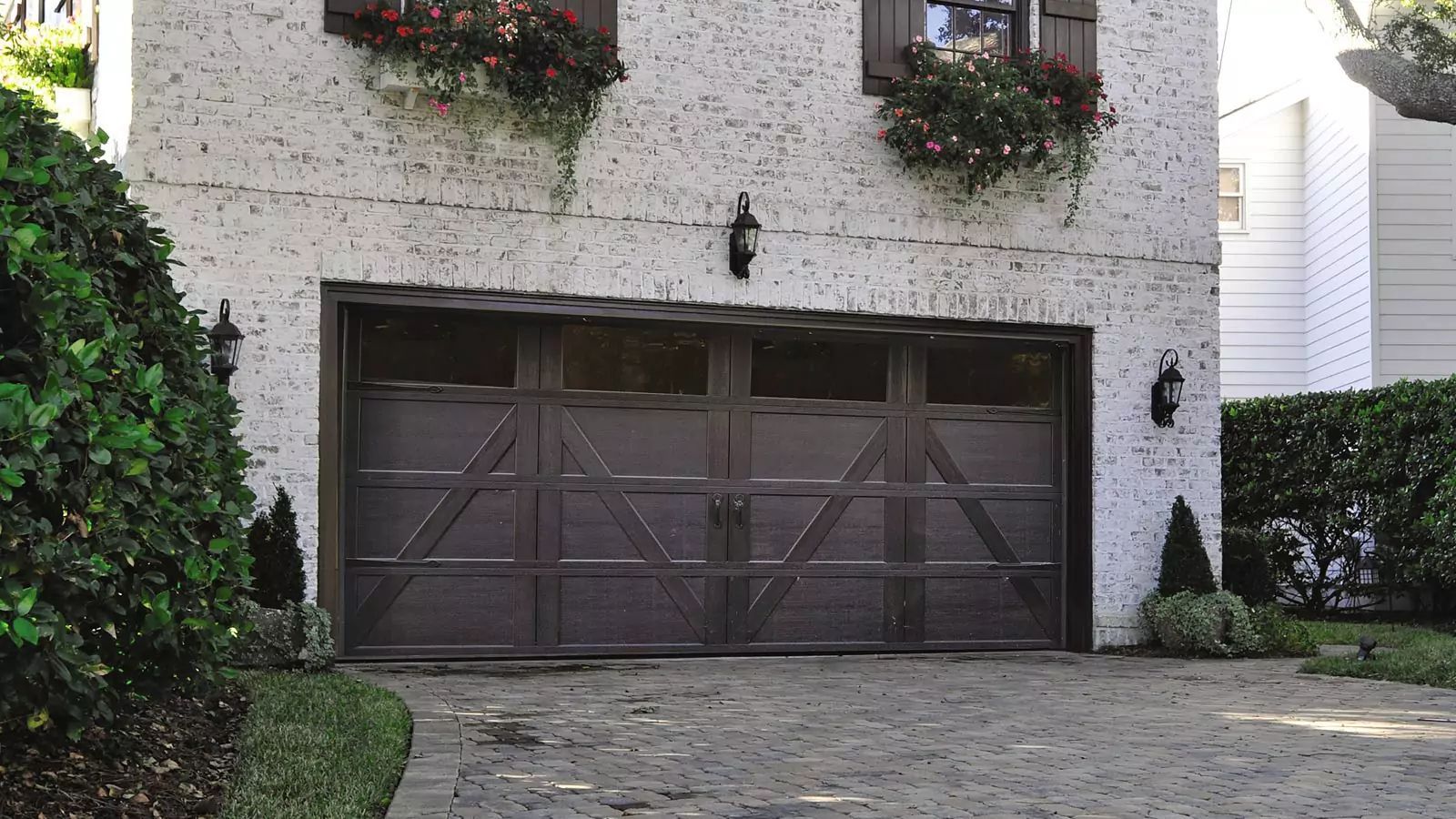 Stone house with a dark wooden garage door, flower boxes, and a cobblestone driveway