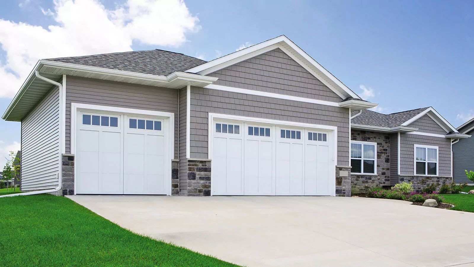 Suburban house with two white garage doors, stone accents, and a clean concrete driveway