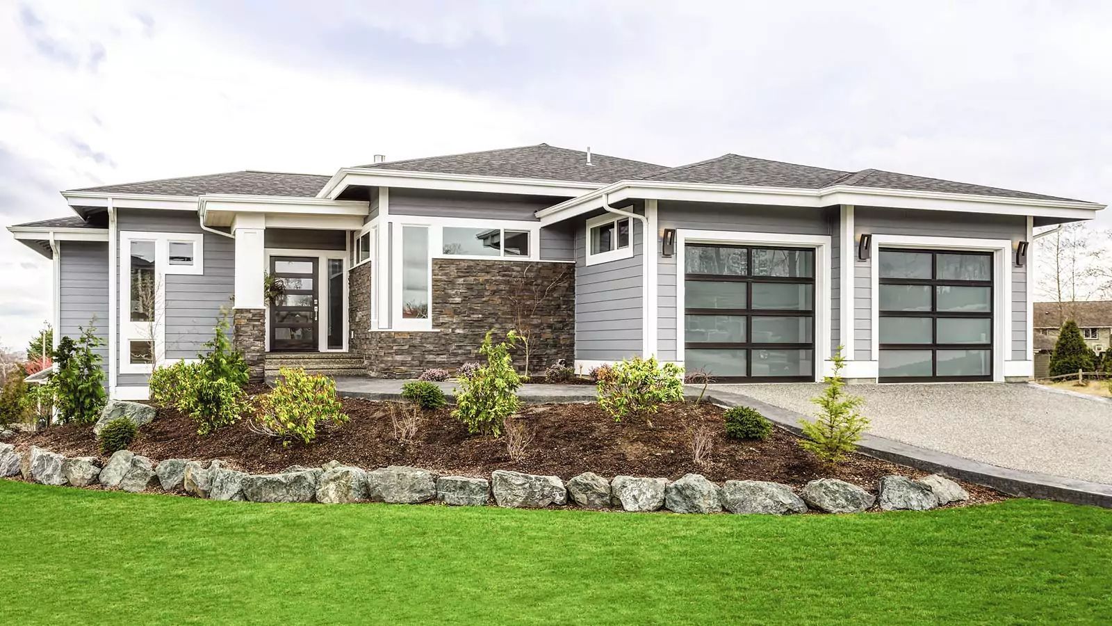 Modern single-story house with stone accents, double garage, landscaped front yard, and green lawn