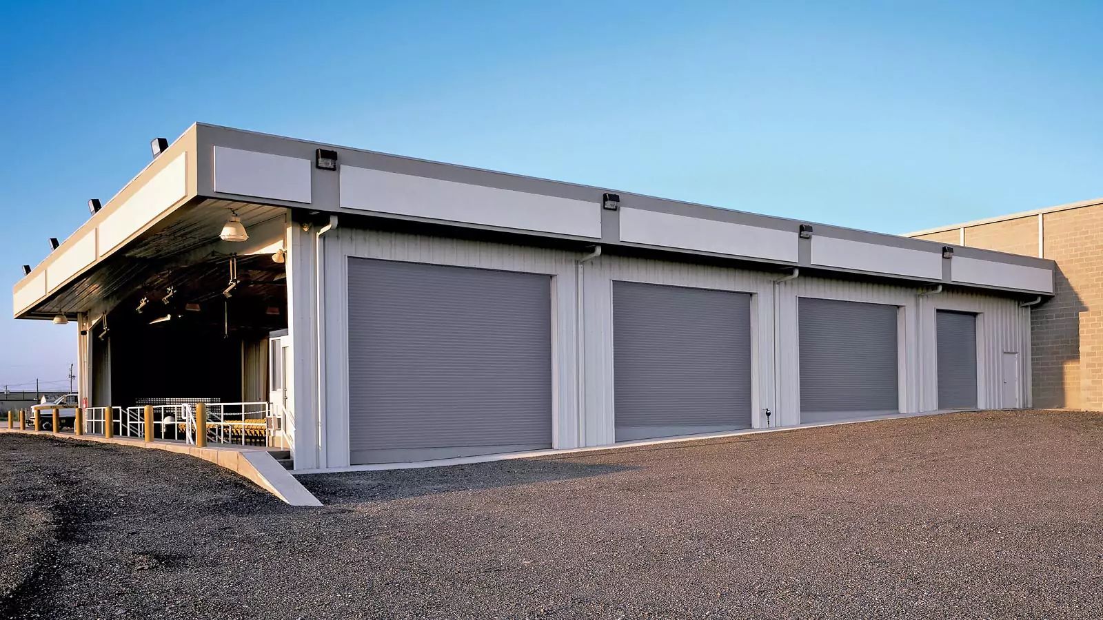 Closed storefront with gray roll-down shutters on a gravel lot under a covered walkway