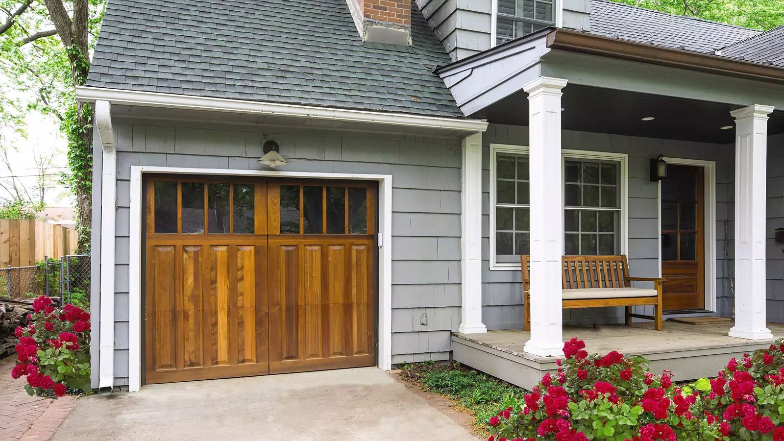 White house exterior with a wooden garage door, front porch, and red flowers along the walkway