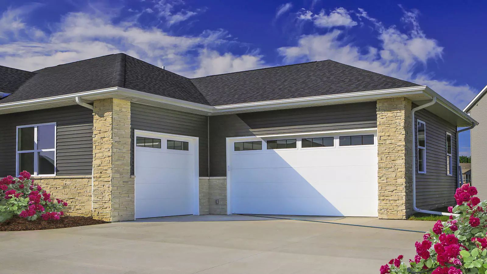 Modern single-story house with brick exterior, two white garage doors, and pink flowers by the driveway