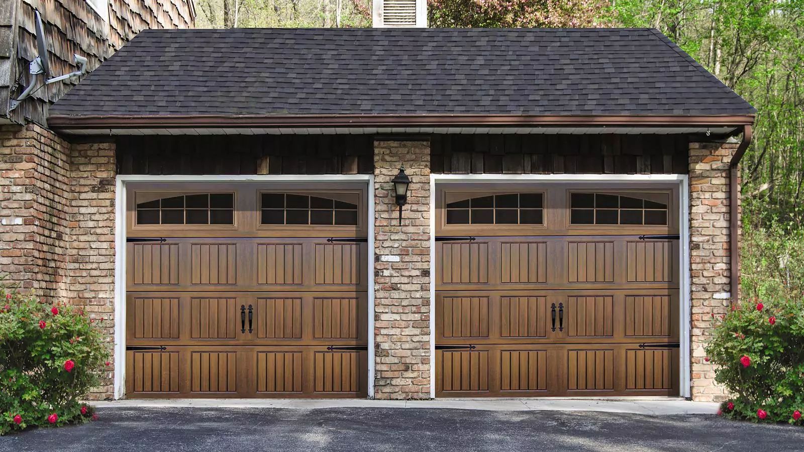 Two-car garage with wooden doors, stone walls, and dark shingled roof