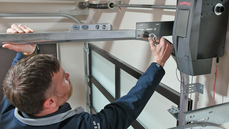 Technician adjusting a garage door opener mechanism with a wrench in a workshop.