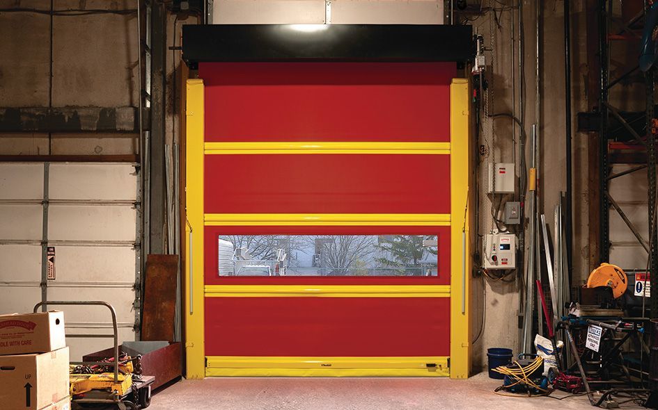 Red industrial garage door with yellow stripes and a small window in a warehouse interior