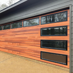 Modern garage door with warm wood panels and black windows on a gray house exterior