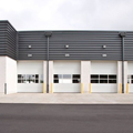 Row of white and gray industrial garage doors on a commercial building facing a paved lot