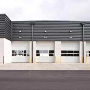 Row of white and gray industrial garage doors on a commercial building facing a paved lot