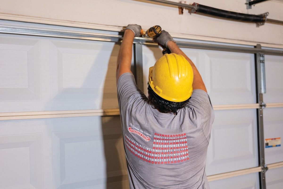 Worker in yellow hard hat installing a garage door opener on a white garage door track