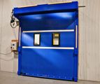 Blue industrial roll-up door with two small windows in a warehouse setting