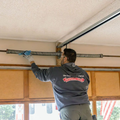 Worker adjusting a ceiling-mounted garage door track with a blue tool in a garage.