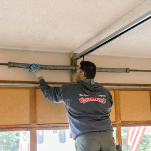 Worker adjusting a ceiling-mounted garage door track with a blue tool in a garage.