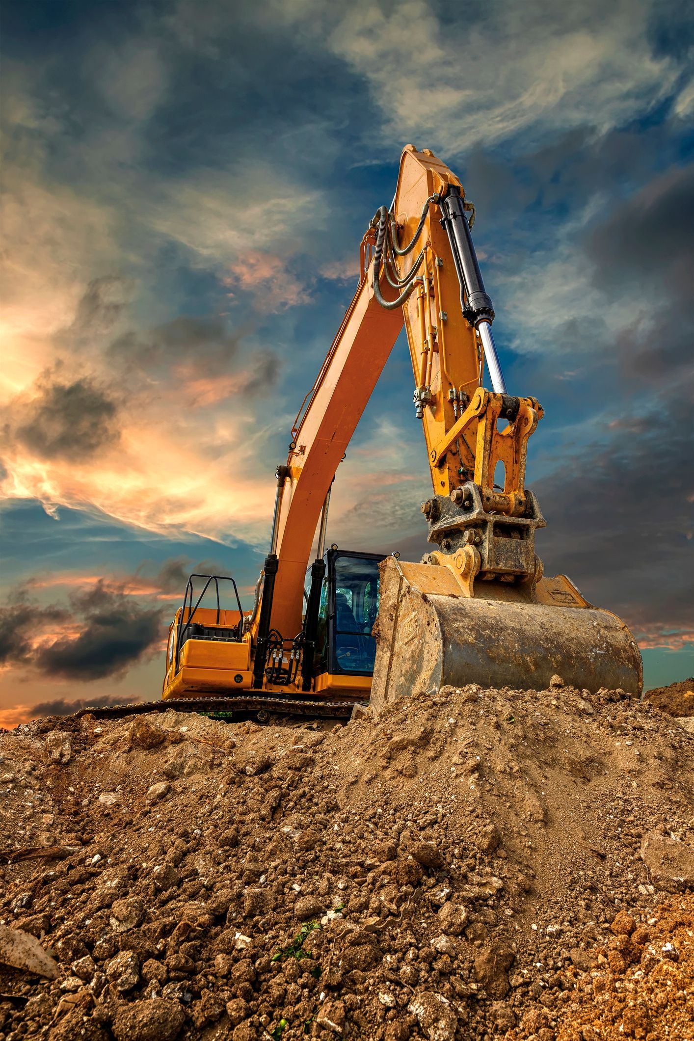 A yellow excavator is sitting on top of a pile of dirt.