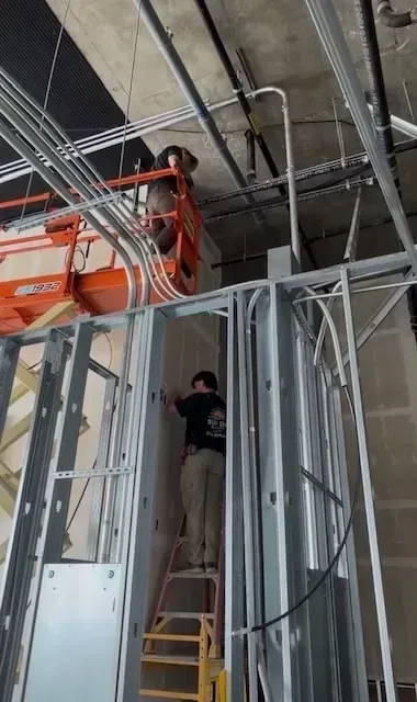 Construction workers on ladders installing framing and cables in a building under construction