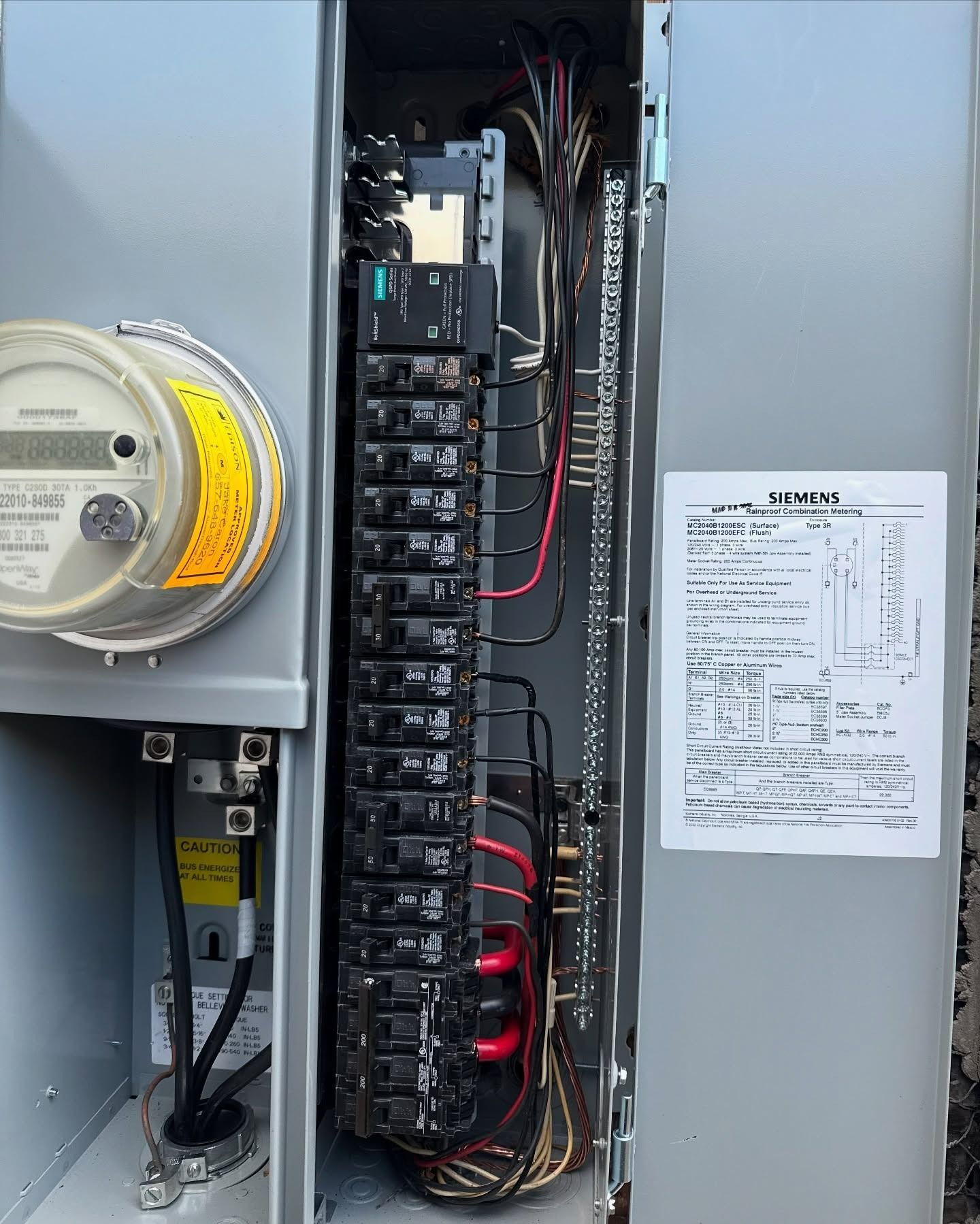 Open electrical panel with wiring, breakers, and a posted inspection sheet on the door.