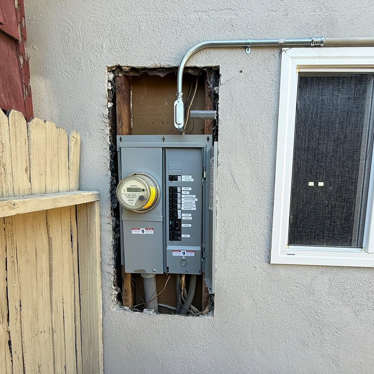 Electric meter and breaker panel mounted on an exterior stucco wall with exposed wiring.