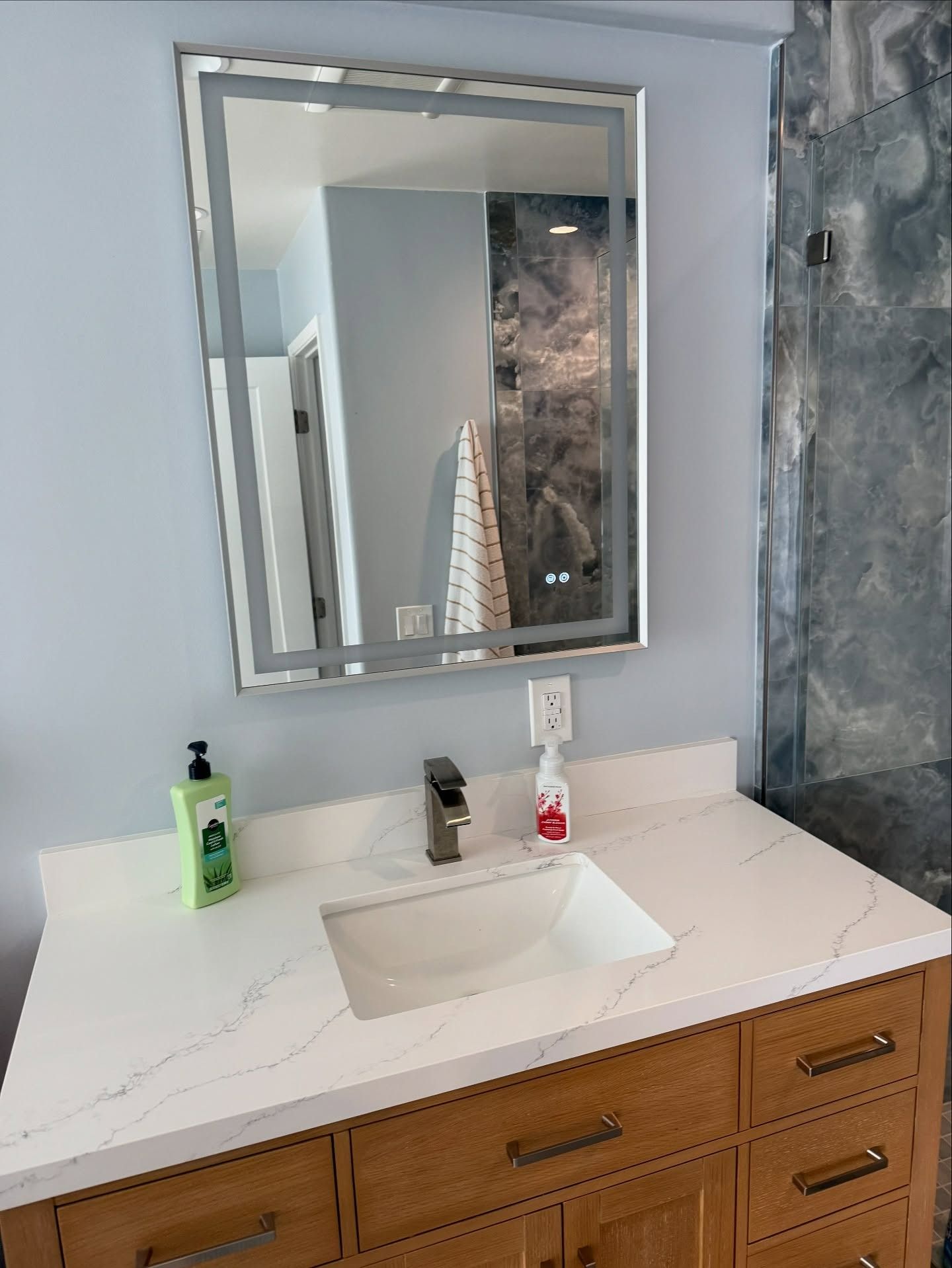 Bathroom vanity with white countertop, wood drawers, sink, mirror, and soap dispensers.