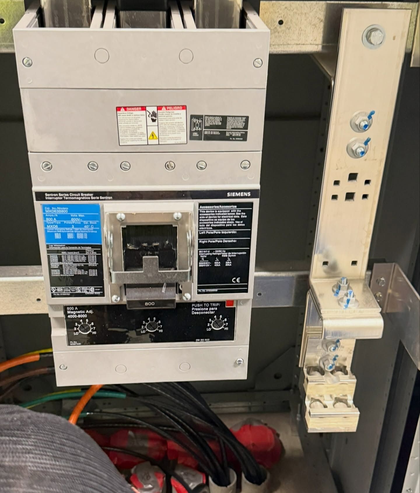 Electrical breaker panel with open cover, wiring, and adjacent control switches in an industrial setting