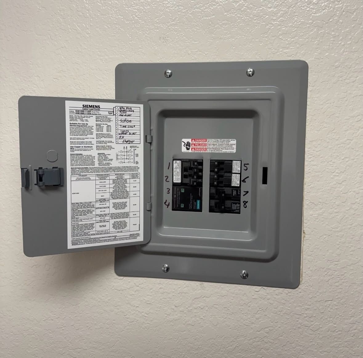 Open electrical breaker panel with door ajar on a beige wall