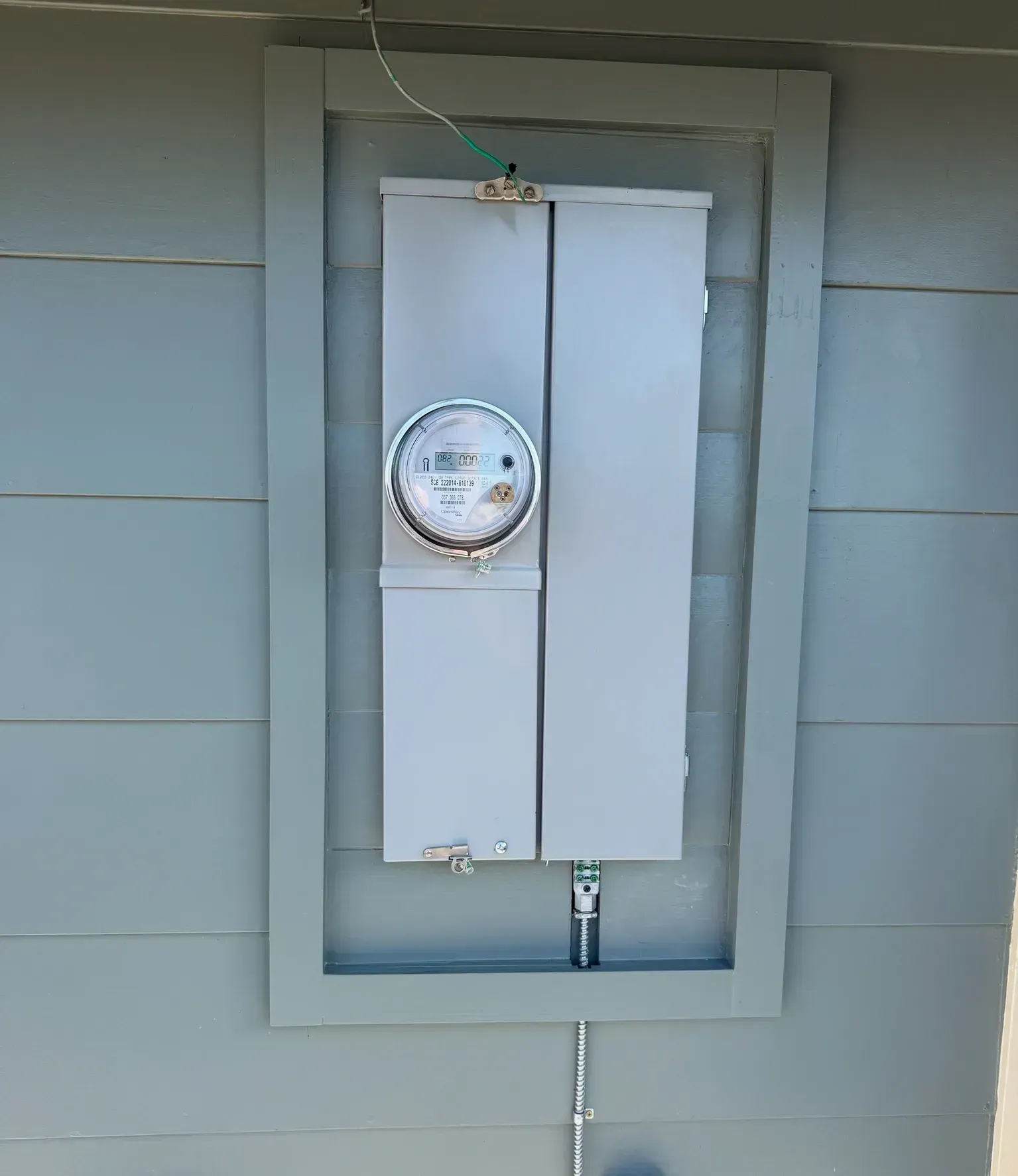 Electric meter mounted on a gray exterior wall in a recessed white utility box
