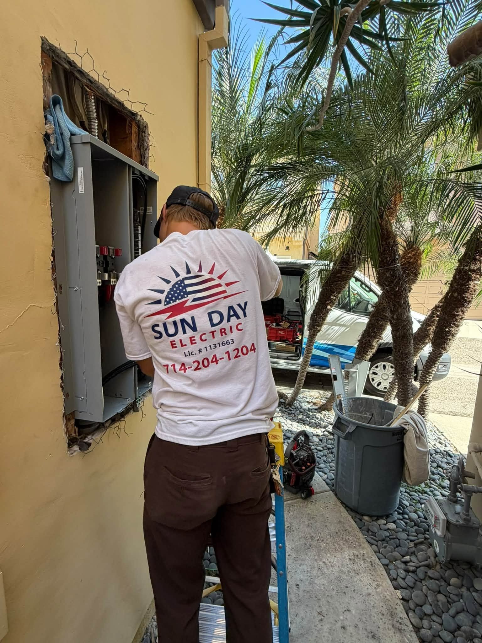 Worker in white Sun Day shirt painting an exterior wall beside a doorway.