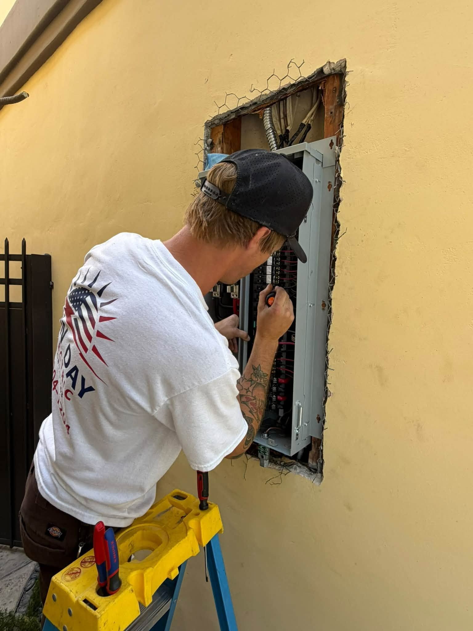 Worker installing an electrical panel in a yellow exterior wall opening