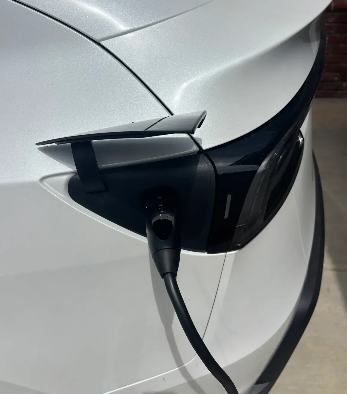 Electric car charging with a plugged-in connector at the front port, white vehicle close-up