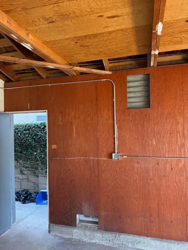 Wood-paneled interior wall with exposed wooden ceiling beams and an open doorway to a courtyard.