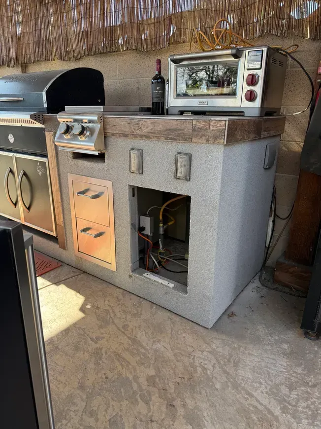 Outdoor kitchen with built-in grill, oven, and storage cabinets under a thatched roof.