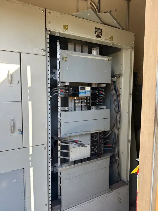 Open electrical panel cabinet with exposed wiring and circuit breakers indoors