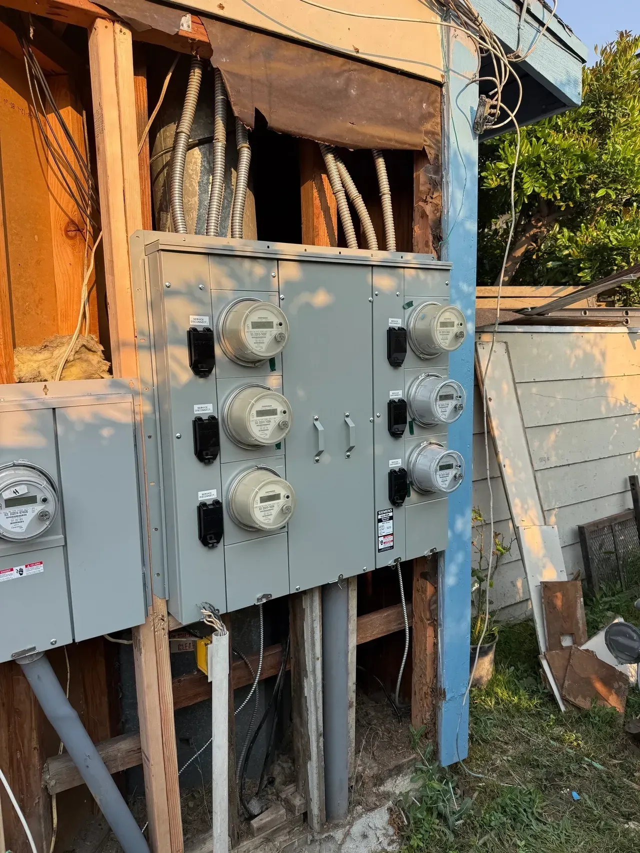 Outdoor electrical breaker panels mounted on a weathered wall with exposed wiring and conduit.