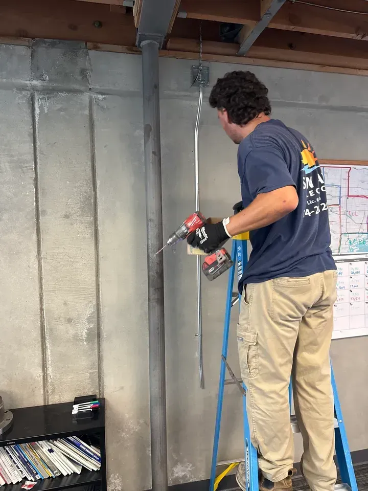 Worker using a power drill on a concrete wall in an unfinished basement