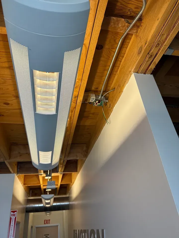 Ceiling-mounted linear light fixture in a modern hallway with exposed beams and white walls
