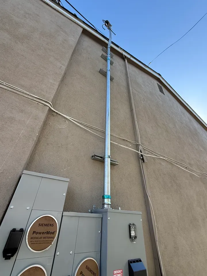 Exterior wall with a tall blue pipe, utility boxes, cables, and a door near the bottom.
