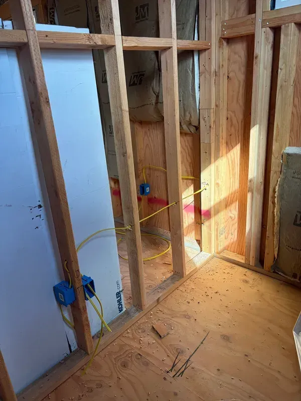 Interior wall framing under construction with exposed studs, electrical boxes, and sunlight on the floor.