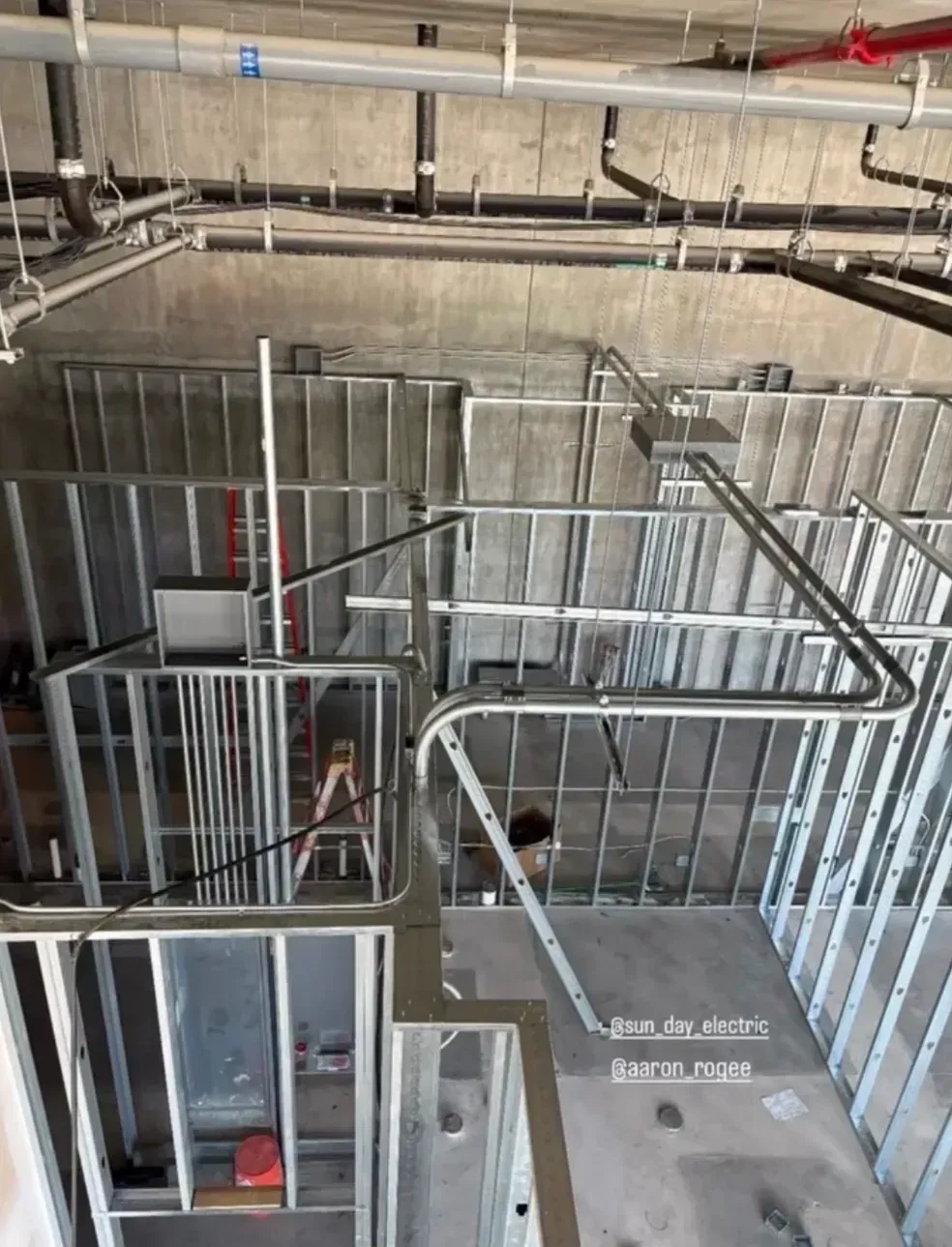 Construction site with metal framing, railings, and exposed ceiling pipes in a gray interior.