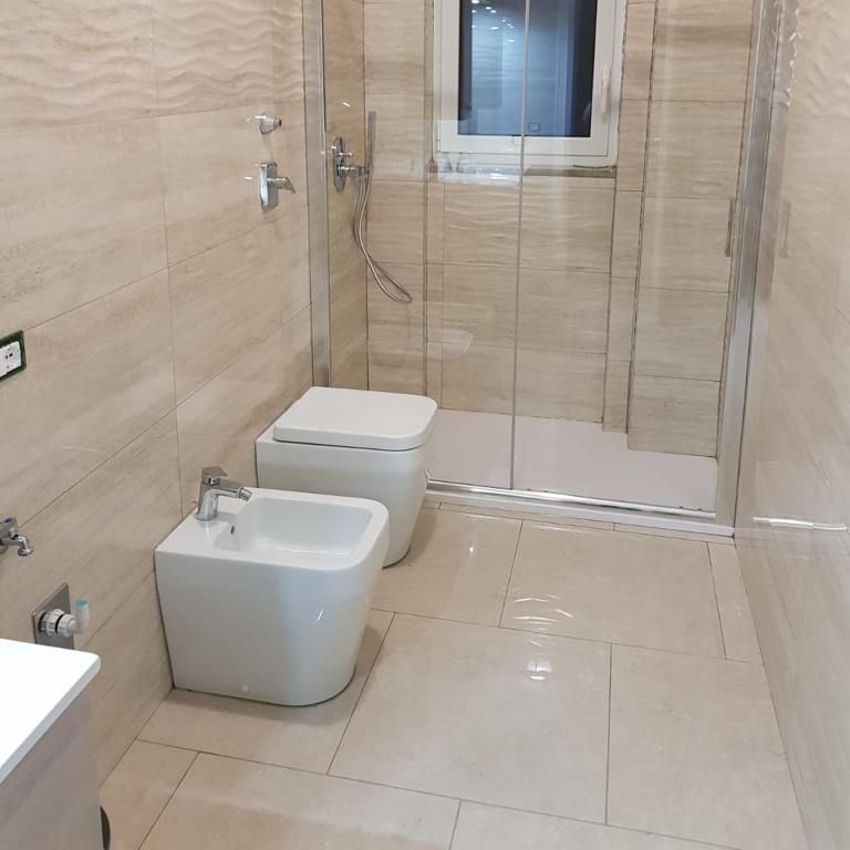 Bagno moderno con pareti piastrellate, WC, bidet e box doccia.