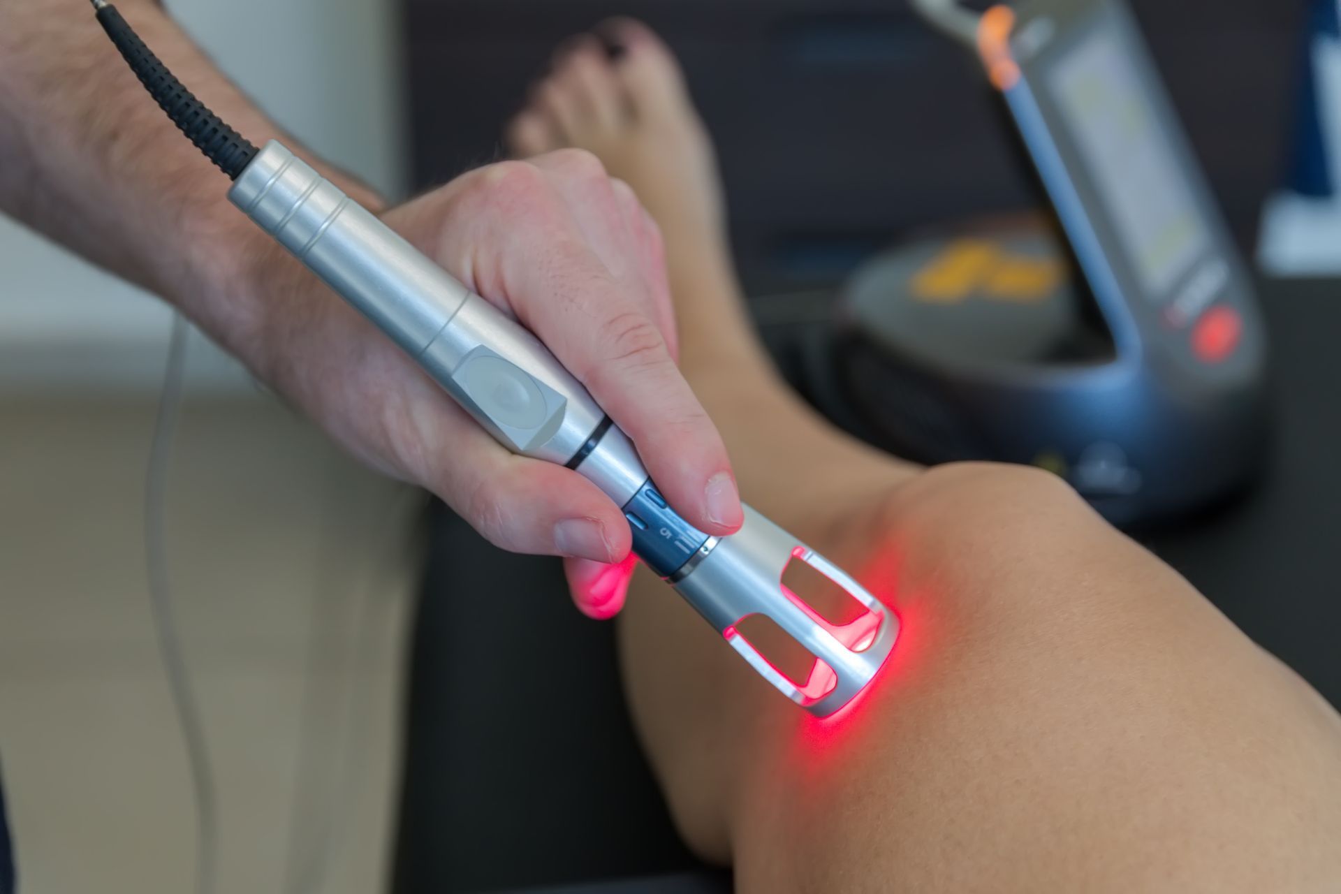 Handheld laser device treating skin on a person’s leg with red light in a spa setting. Handheld laser device treating skin on a person’s leg with red light in a spa setting.