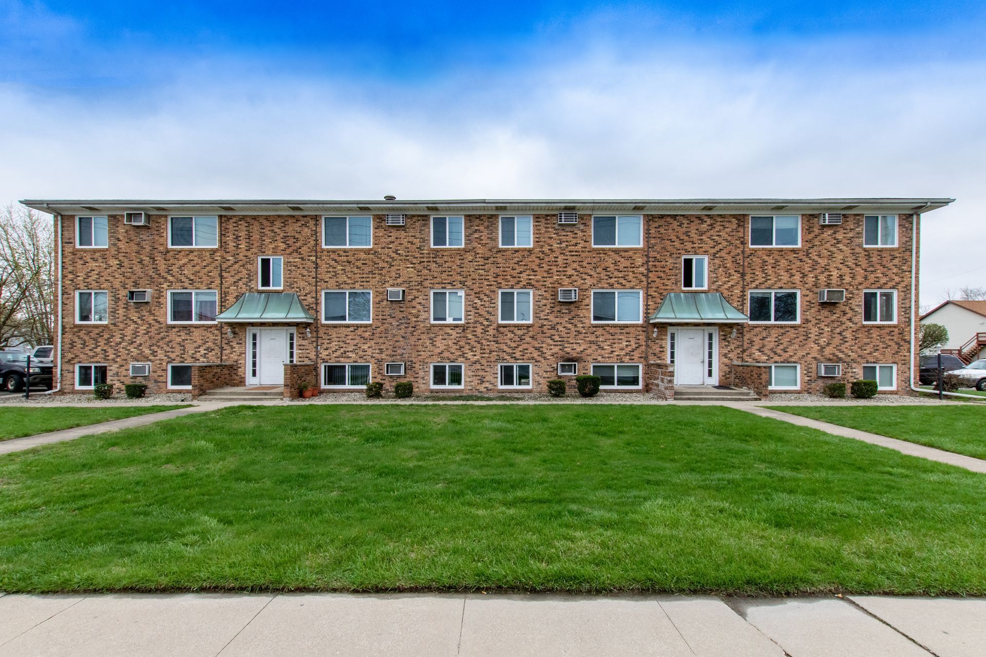 Two-story brick apartment building with green lawn and blue sky.