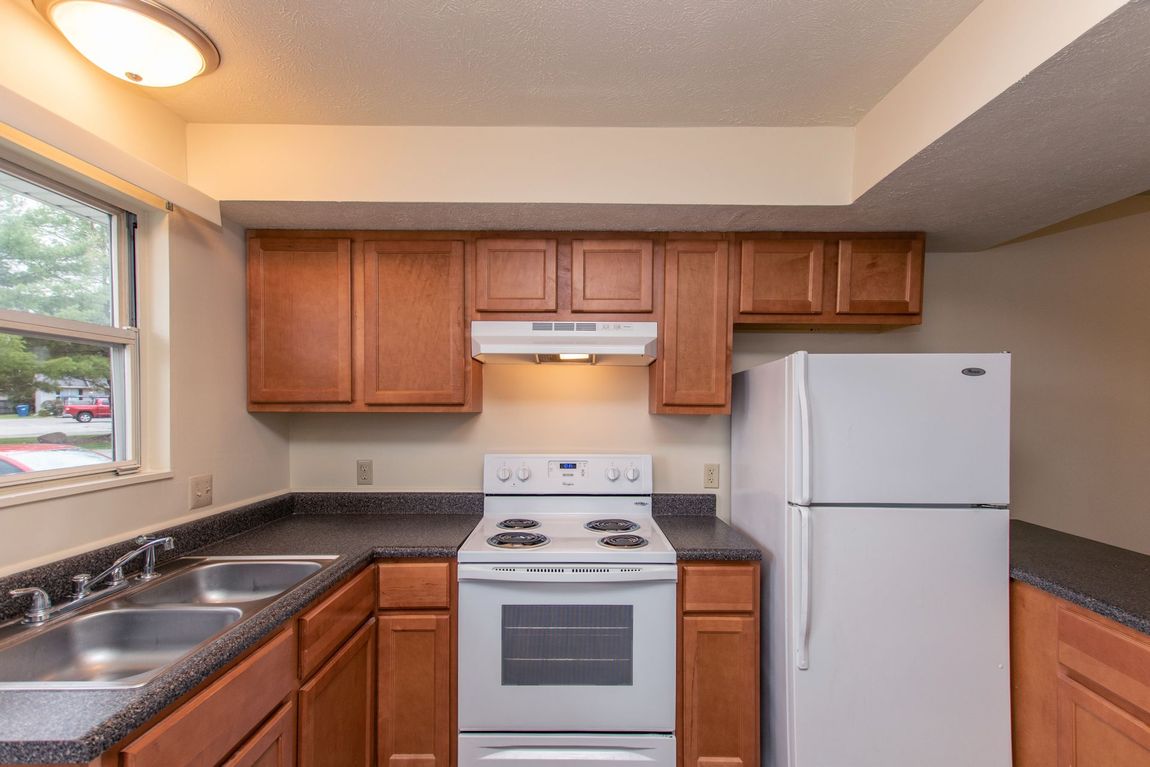 Kitchen with wood cabinets, white appliances, and a black countertop next to a window.