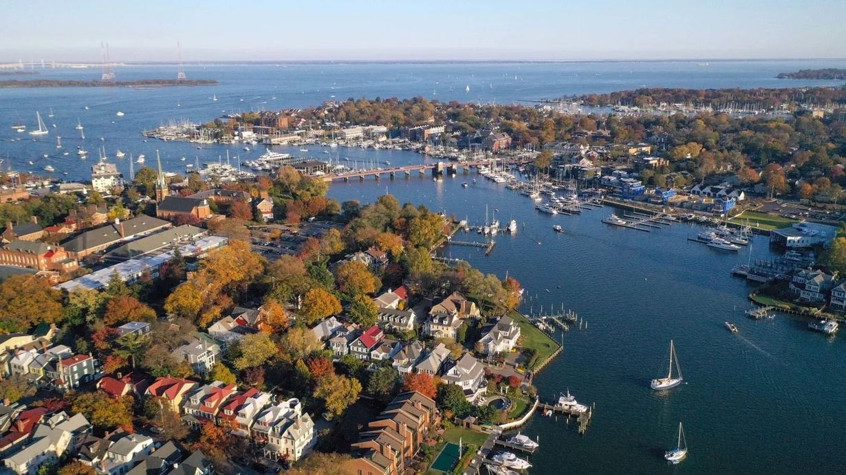 Aerial view of a coastal town with boats in a marina and autumn-colored houses along the shoreline