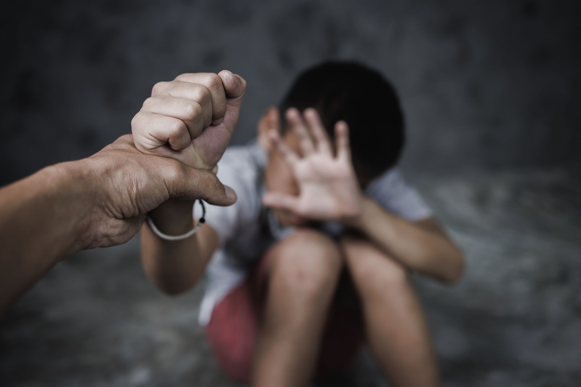 Hand holding a knife toward a frightened person covering their face in a dark room