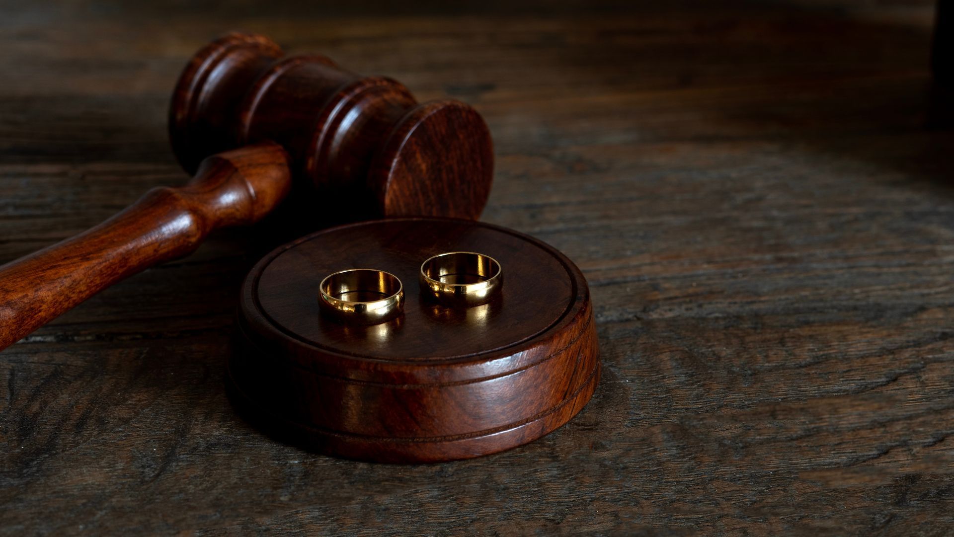 Wedding rings on a wooden gavel and base, symbolizing a marriage or legal union.