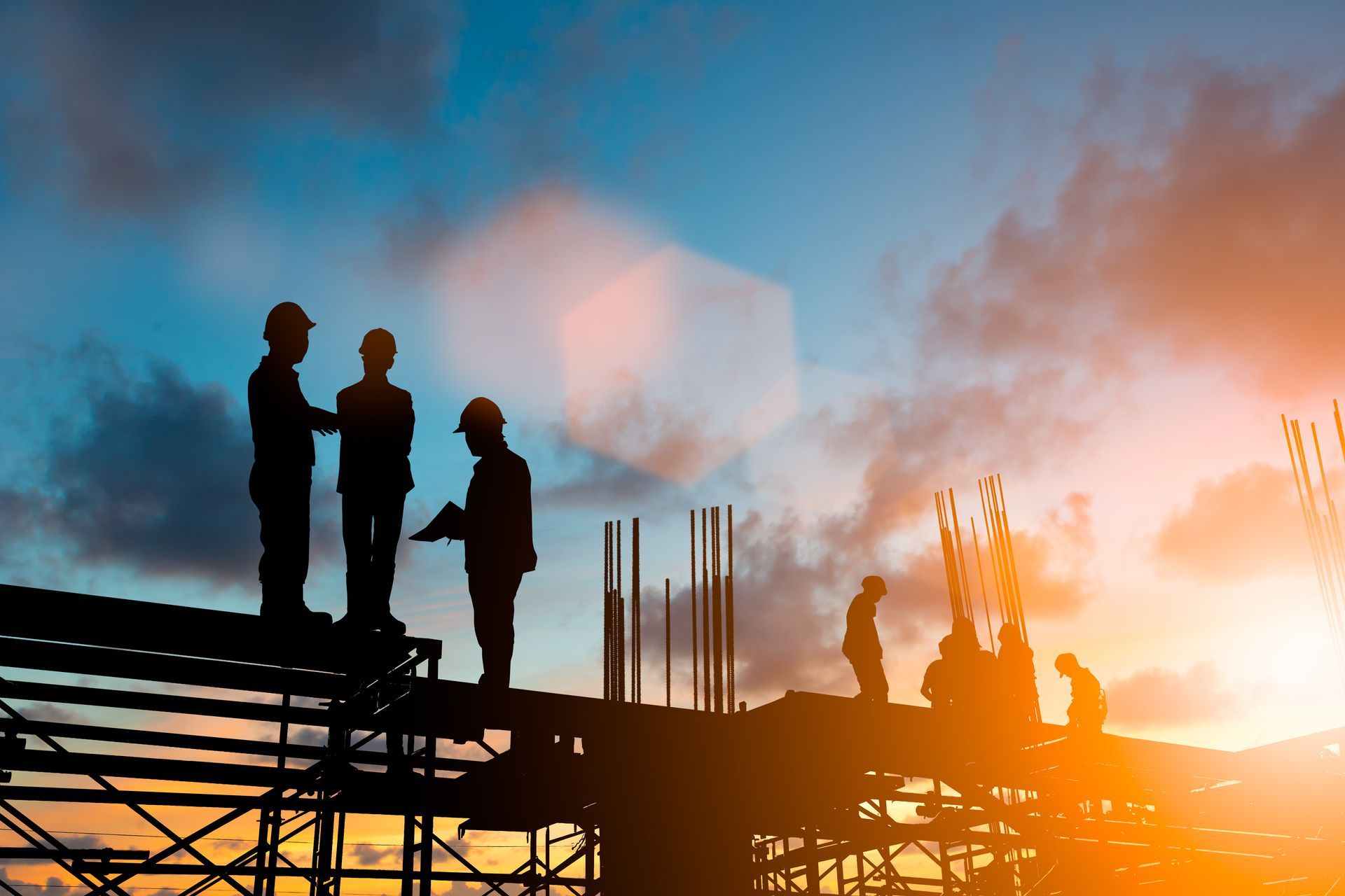 Silhouettes of construction workers on a scaffold against a vibrant sunset sky.