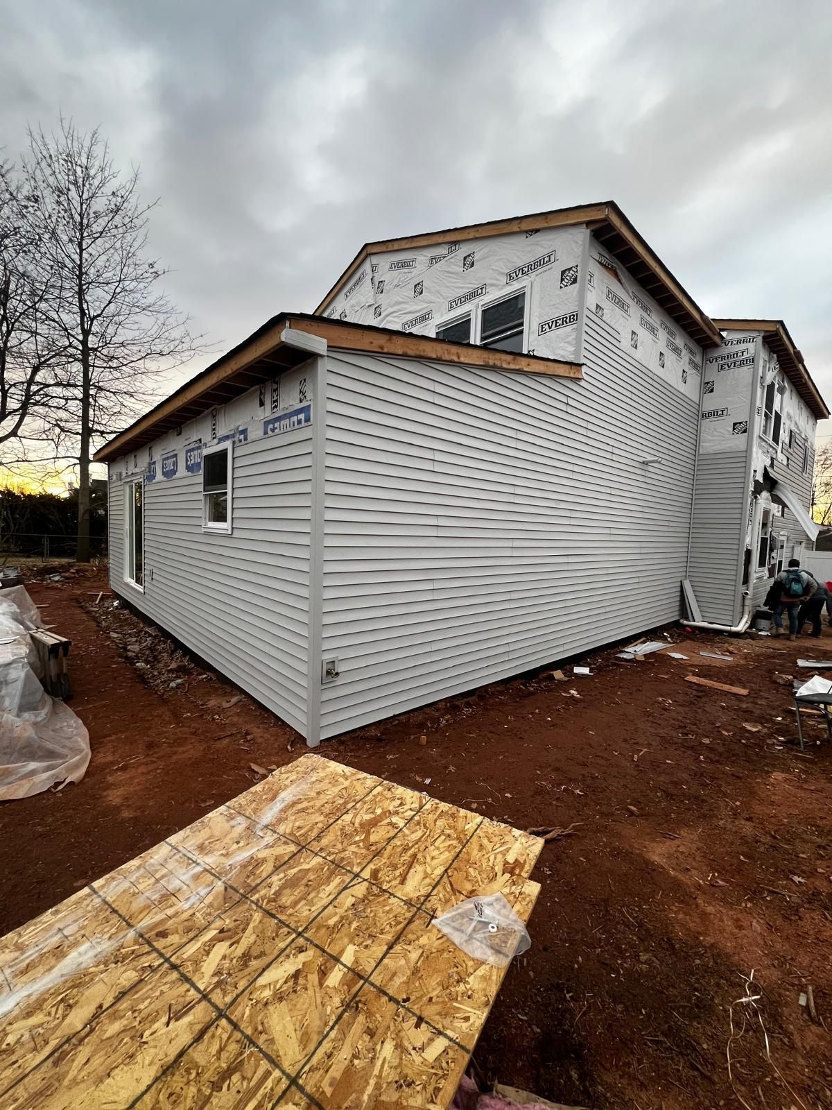 A house under construction with light-colored siding on the lower level and protective house wrap on the upper section.