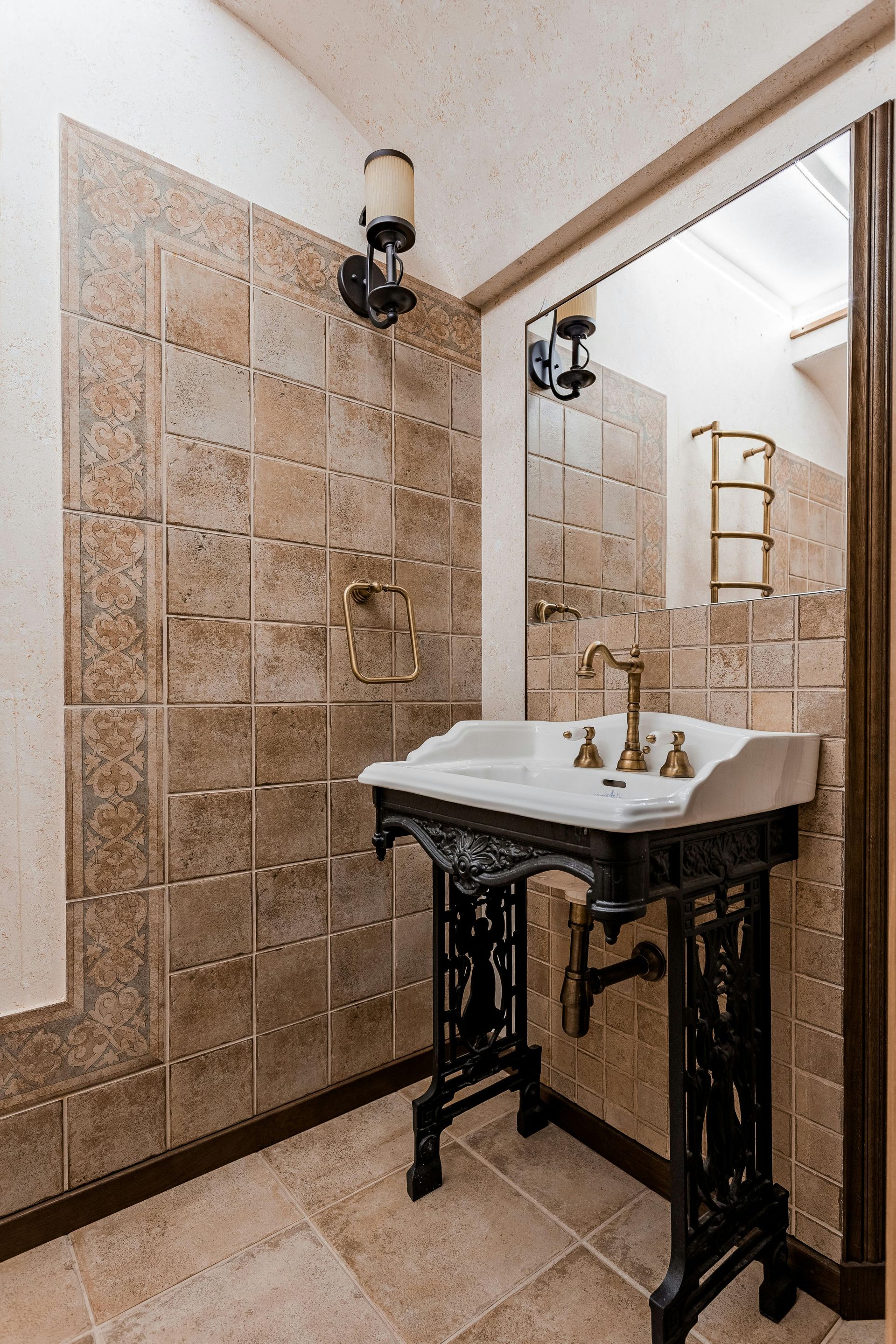 Small tiled bathroom with a pedestal sink, mirror, wall sconce, and ladder shelf.