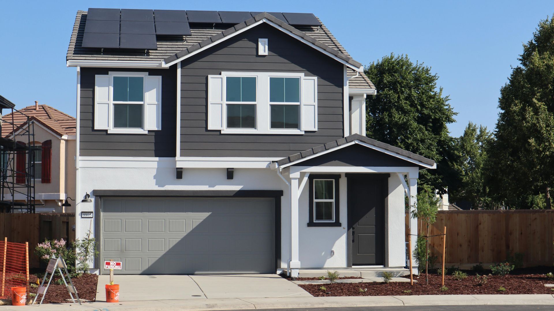 Modern two-story gray house with solar panels, white trim, and a two-car garage under a clear blue sky
