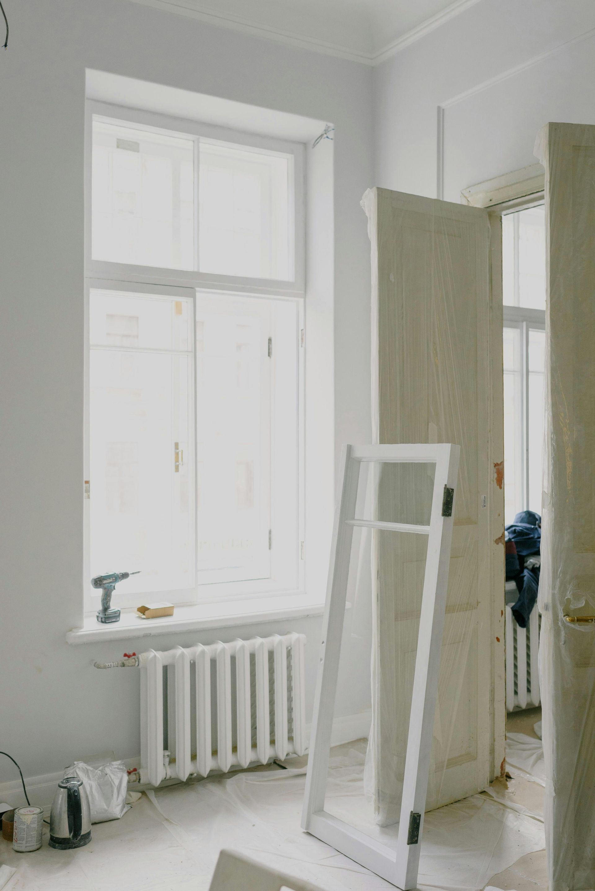 Bright room with a window, radiator, and a leaning mirror near a wardrobe and clothes rack