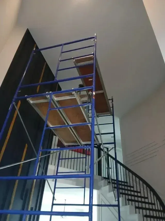 Burleson electrician - A blue scaffolding tower stands in a spacious interior, reaching towards the high ceiling above a staircase.