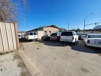 Burleson Electrician - Parking lot with several cars lined up in front of a brick building on a clear day. Sparse vegetation and a utility pole frame the scene.